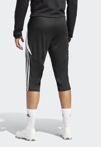 Svarte idrettsshorts med hvite side-striper, tettsittende design, kne-lengde, laget av glatt stoff, kombinert med hvite sokker og fotballsko.