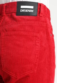 Pantaloni in corduroy rossi con superficie strutturata, tasche posteriori e etichetta nera con logo in vita.