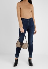 Tan fitted turtleneck sweater, dark blue skinny jeans with rolled cuffs, black ankle boots, and a patterned handbag with a brown strap.