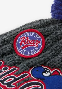 Un bonnet en tricot gris avec un patch rond rouge portant "Kings of Roar" et des accents bleus, surmonté d'un pompon bleu duveteux.