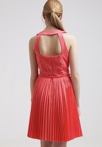 Koronowy, plisowany sukienka bez rękawów, z odkrytymi plecami i haftowanymi detalami na biuście. Gładka tekstura i dopasowana talia.