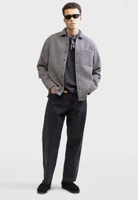 Grå ternet skjortejakke, sort t-shirt, mørke denimbukser og sorte sko. Accessories inkluderer solbriller og et mønstret bandana.