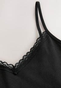 Camiseta sin mangas negra con escote en V, con delicado borde de encaje festoneado a lo largo del escote y tirantes ajustables. Textura de tela suave.