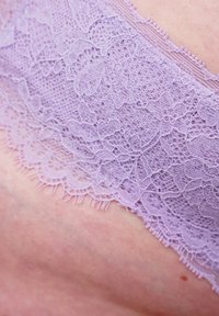 Lavendelspitzenstoff zeigt filigrane Blumenmuster mit gewellten Kanten; die weiche Textur verstärkt die visuelle Detailgenauigkeit und das Design.