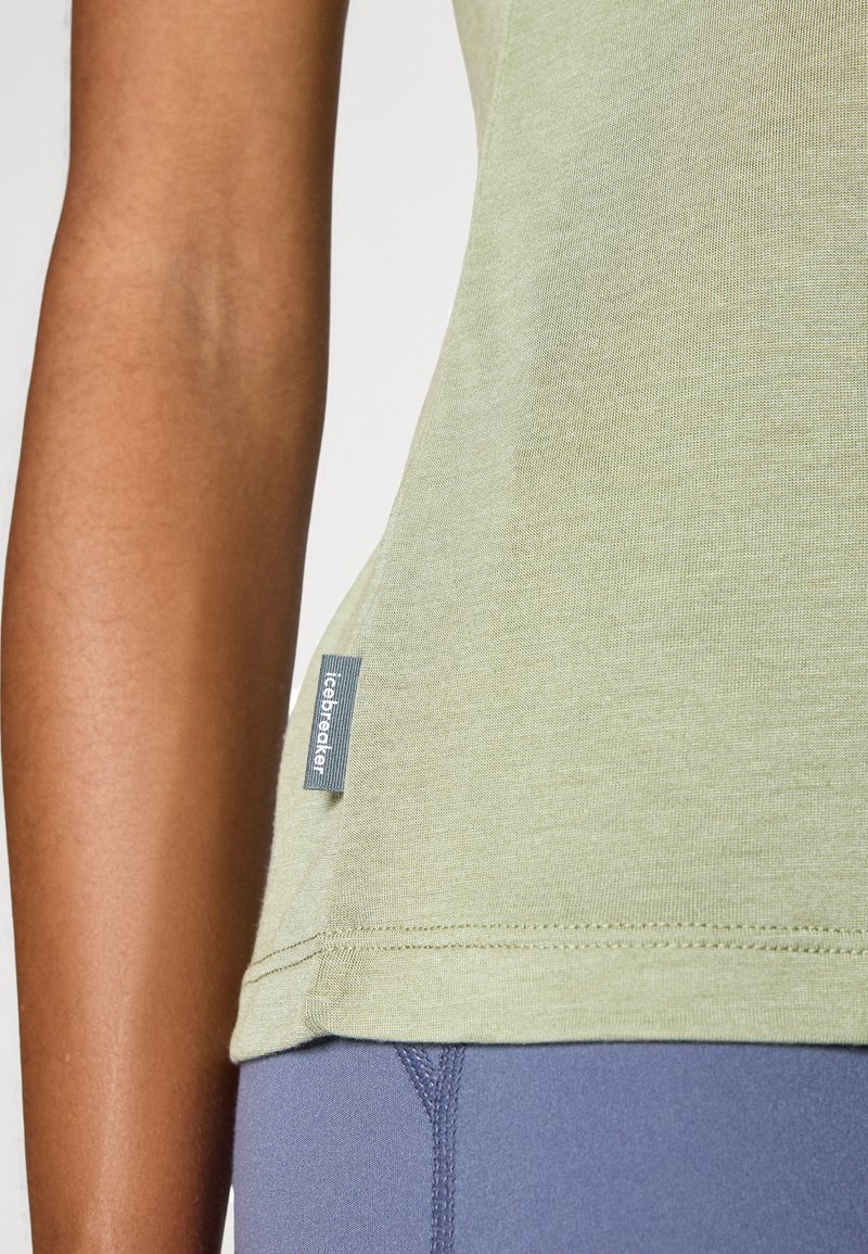 Nahaufnahme einer Person, die ein hellgrünes Shirt mit einem Icebreaker-Label und blaue Hosen trägt, wobei ein Teil des Arms und des Oberkörpers zu sehen ist.