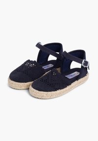 Námornícke espadrilky so sieťovinovou vrchnou časťou, zaoblenou špičkou, remienkom okolo členka so sponou a podrážkou z juty. Zložitý výrezový dizajn na vrchnej časti.