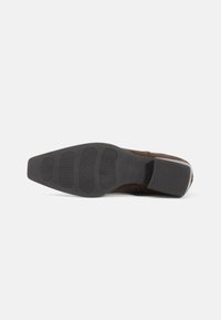 Chaussure en daim marron avec une semelle en caoutchouc texturée. La semelle présente des rainures horizontales pour une meilleure adhérence et un design de bout carré.