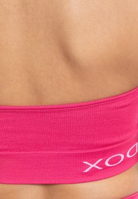 Sostén deportivo rosa con textura acanalada y acento de logo blanco, que presenta un diseño sin costuras y una textura suave, mostrando la parte trasera desde un ángulo cercano.