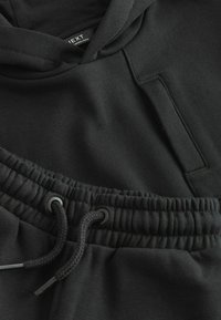 Ensemble de sweat à capuche noir et de pantalon de jogging, fabriqué en tissu doux. Les caractéristiques incluent une poche avant, un cordon de serrage ajustable et une taille élastique.