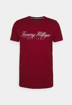 T-shirt in cotone rosso a maniche corte, con scritta corsiva bianca "Tommy Hilfiger EST. 1985" sul petto. Design pulito, scollatura rotonda.