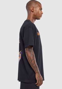 Black oversized t-shirt featuring short sleeves, crew neck, and orange graphic text on the front. Smooth cotton fabric with a relaxed fit.