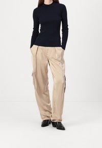 Marinblå ribbad långärmad topp kombinerad med beigefärgade satinkargo-byxor som har sidfickor, raka ben och svarta klackskor.