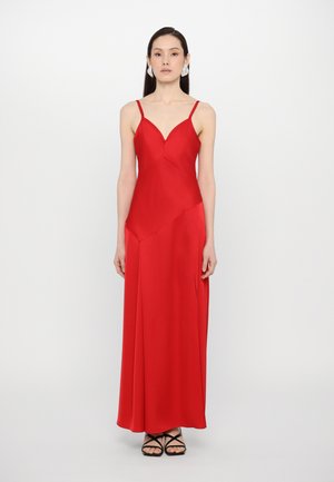 Red satin evening dress with a fitted bodice, V-neckline, and thin straps. Features a flowy skirt with an asymmetric hem. Worn with black strappy shoes.