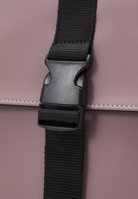 Pink bag section featuring a black plastic buckle and a woven strap, emphasizing the contrast between the materials and colors.