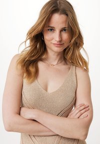 Beżowy, dzianinowy top bez rękawów z dekoltem w serek, z otwartymi detalami. Gładka faktura z luźnym krojem, zestawiony z minimalistyczną biżuterią w kolorze złotym.