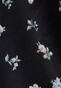 Svart tyg med ett delikat blommönster, som har små beige och ljusblå blommor samt gröna blad på en texturerad bakgrund.