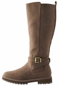 Botte haute en cuir marron avec une lanière latérale et une boucle en laiton, semelle plate à relief et languette de traction en haut à l'arrière.