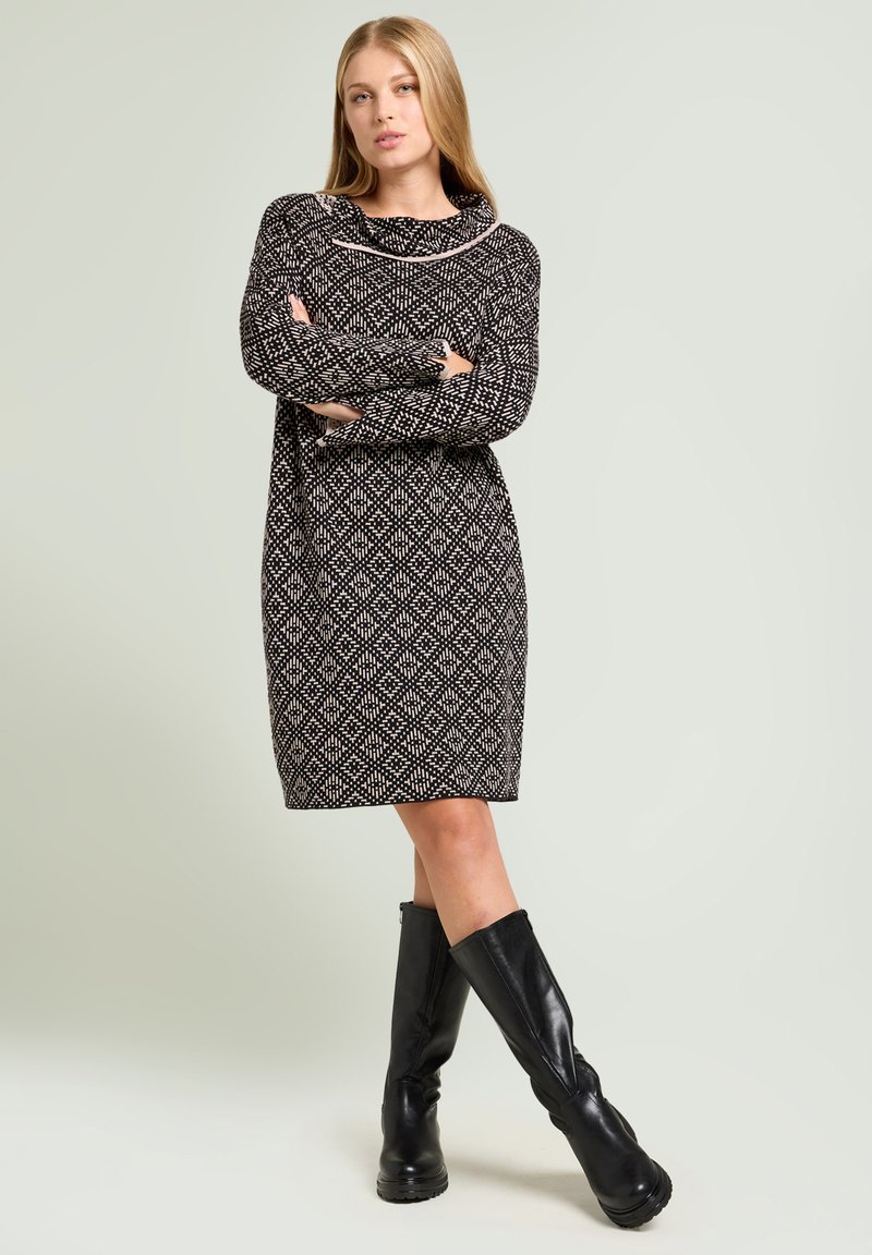 Zwart-wit gebreide jurksweater met een losse pasvorm, lange mouwen en een textuurrijke stof, gecombineerd met kniehoge zwarte leren laarzen.