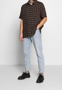 Camisetta nera a maniche corte con un motivo geometrico, abbinata a jeans azzurri a sigaretta e scarpe stringate nere.