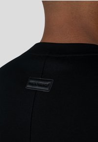 Czarna koszulka z krótkim rękawem z prążkowanym kołnierzykiem oraz małą czarną skórzaną metką z wytłoczonym tekstem na tylnej części kołnierza.