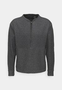 Šedý dlouhý rukáv pulovr s polo zipem, vyrobený z měkké tkaniny. Obsahuje ploché švy a hladký povrch. Jednoduchý, minimalistický design.