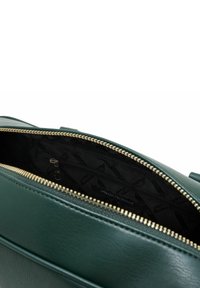Borsa in pelle verde con zip, aperta per mostrare l'interno nero con il motivo del logo Armani Exchange e una tasca interna con zip.