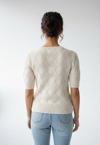 Sweter dziergany w kolorze kremowym, z teksturowanym wzorem diamentowym, krótkimi rękawami i prążkowanym dołem. Widok od tyłu.