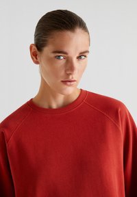 Rode sweatshirt met een ronde halslijn, raglanmouwen en een gladde textuur. Minimalistisch ontwerp zonder extra patronen of accenten.