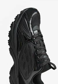 Čierna atletická obuv s kombináciou hladkých a textúrovaných materiálov, polstrovaným golierom a vzorovanou podrážkou pre trakciu.