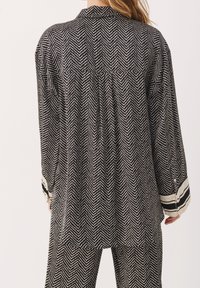 Tenue à motif en chevrons noir et blanc avec une coupe ample, comprenant une chemise à col et un pantalon large avec des accents rayés.