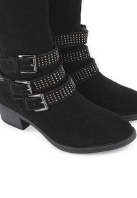 Botas de tobillo de ante negro con tres correas ajustables adornadas con tachuelas y hebillas plateadas, tacones de bloque bajos y diseño de punta redonda.