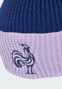 Knitted beanie in navy and lavender, featuring a striped rooster logo in dark blue on the lavender band. Soft, textured fabric.
