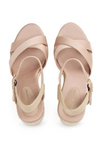Beige espadrille sandals featuring wide cross straps, a textured fabric base, and a small buckle on ankle strap. Smooth finish, canvas insole.
