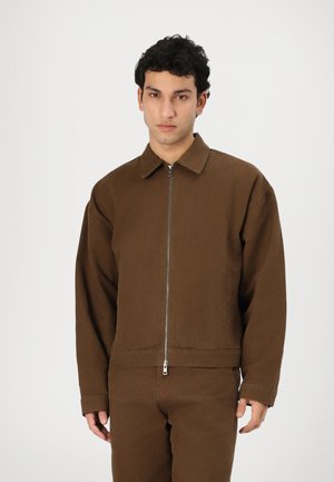 Brown cotton jacket with a zip front, point collar, and long sleeves. It features a relaxed fit and subtle stitching details.