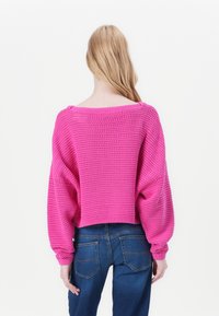 Pull en tricot rose à coupe ample, encolure dégagée et motif texturé. Associé à un jean en denim bleu, montrant la vue arrière et un tissu doux.