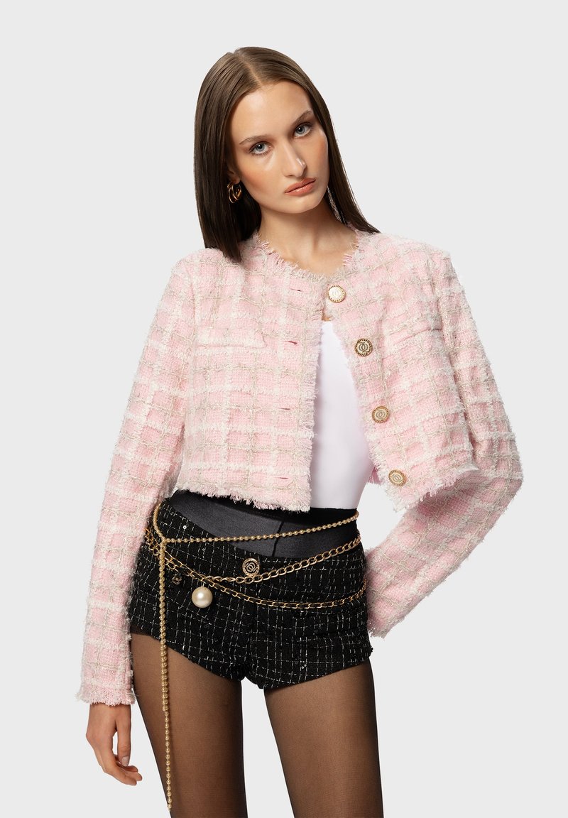Pink tweed cropped jacket featuring a textured grid pattern, frayed edges, and gold button closures. Worn with a black chain-accented belt.