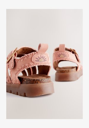 Sandale din material textil roz, cu detalii împletite, talpă căptușită din plută și broderie cu soare pe barete. Închidere cu cataramă ajustabilă.