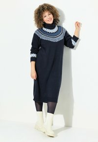Abito in maglia navy con collo alto, yoke a motivo blu e bianco, maniche lunghe e orlo a coste. Abbinato a stivali bianchi alla caviglia.