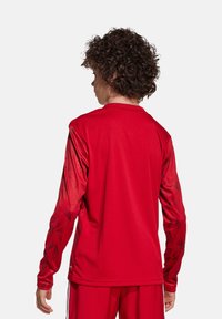 Maglietta sportiva rossa a maniche lunghe con un design testurizzato sulle maniche, caratterizzata da un colletto rotondo e una vestibilità ampia.