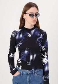 Langermet svart skjorte med blå og hvite abstrakte mønstre, rund hals, fabrikkens tekstur fremstår myk, kombinert med blå denimjeans.