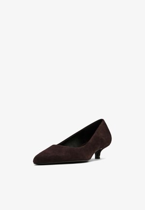 Mørkebrune ruskinds pumps med spids tå og lille hæl. Ydersiden har en glat tekstur, mens indersiden er foret med sort.