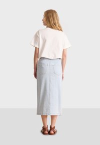 Top bianco a maniche corte abbinato a una gonna midi di denim azzurro chiaro con tasche posteriori, completato da sandali marroni con cinturini.