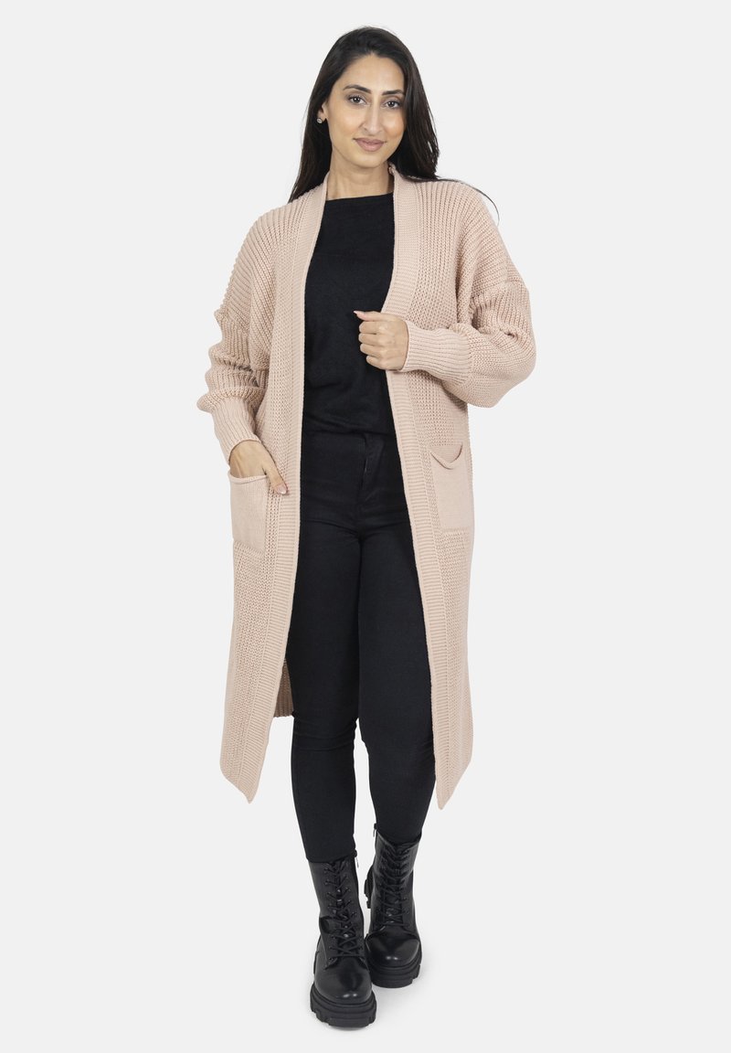 Lång, öppen-front cardigan i ljust beige strukturerad stickning med ribbade detaljer och två framfickor. Bärs över en svart topp och byxor.