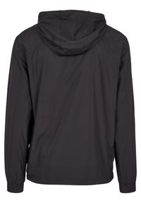 Veste légère noire à manches longues, poignets élastiques et capuche attachée, vue de dos sur fond blanc.