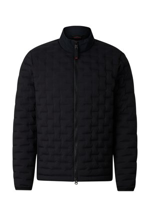 Man wearing black quilted jacket, black pants, black sneakers, and dark sunglasses, standing with one hand in pocket and one hand near collar.