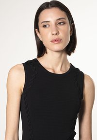 Schwarzes ärmelloses Kleid mit gerippter Struktur und geflochtenen Akzenten an den Seiten. Glatter Stoff mit figurbetontem Schnitt, der die Silhouette zur Geltung bringt.