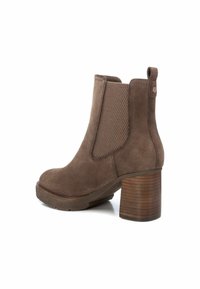 Stivale alla caviglia in suede marrone con tacco in legno impilato, pannelli laterali elasticizzati e finitura testurizzata. Disponibile una linguetta sul retro per facilitare l'indossamento.