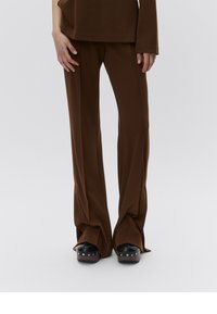 Pantalon marron évasé en tissu lisse et extensible. Il comporte des coutures latérales et est assorti à des chaussures à plateforme noires ornées de clous.