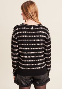 Schwarzer und beiger gestreifter Pullover mit lockerer Passform, gerippten Bündchen und einem Knopfdetail am Rücken des Halsausschnitts. Weicher Strickstoff.
