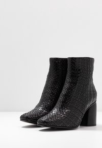 Botas de tobillo negras con un diseño texturizado y trenzado y una punta cuadrada. El tacón ancho proporciona estabilidad. Acabado suave con un aspecto brillante.
